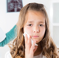 Young girl with soft tissue injury holding cold compress to cheek