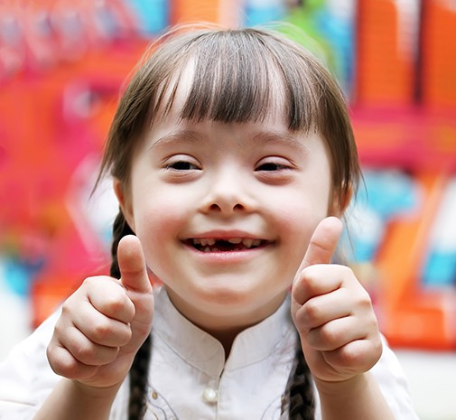 Young girl giving thumbs up after dental treatment for children with sensory issues