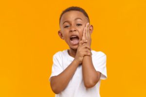 boy holding his face needing baby tooth extraction