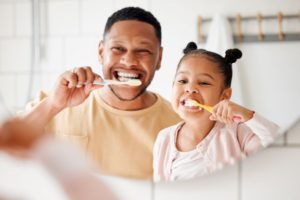 Dad and daughter brushing teeth in front of mirror